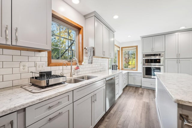 kitchen with wood-type flooring, backsplash, sink, light stone countertops, and appliances with stainless steel finishes