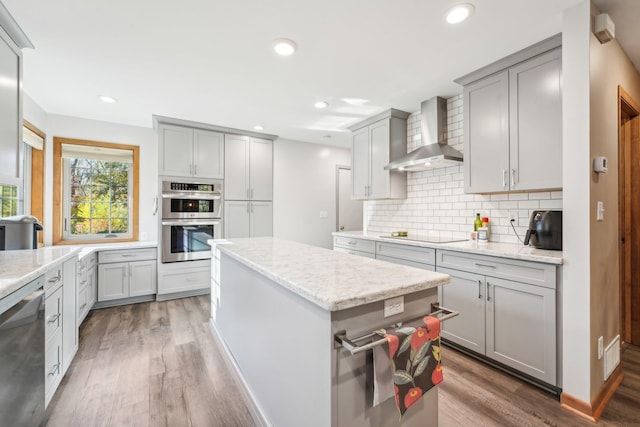 kitchen with a kitchen island, wall chimney range hood, dark hardwood / wood-style floors, appliances with stainless steel finishes, and light stone counters