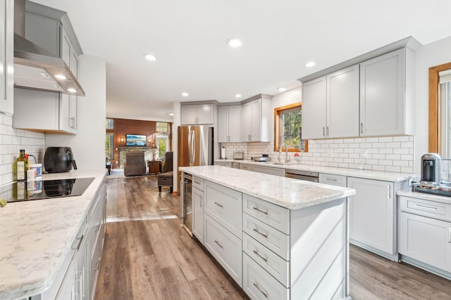 kitchen with wall chimney range hood, light hardwood / wood-style flooring, and a kitchen island