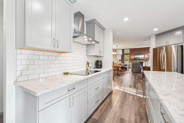 kitchen featuring tasteful backsplash, dark hardwood / wood-style flooring, black electric cooktop, stainless steel fridge, and wall chimney exhaust hood