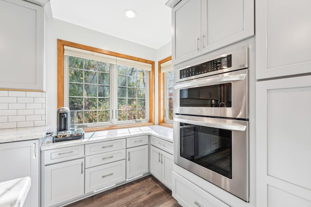 kitchen with white cabinets, tasteful backsplash, dark hardwood / wood-style flooring, light stone counters, and stainless steel double oven