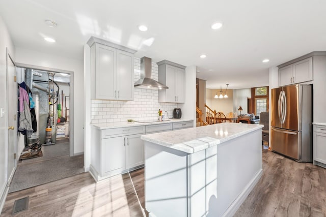 kitchen featuring wall chimney range hood, light hardwood / wood-style flooring, stainless steel fridge, and gray cabinets