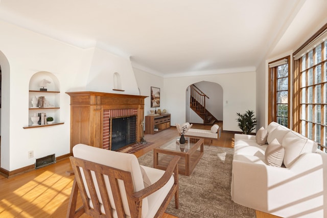 living area featuring a brick fireplace, built in shelves, wood finished floors, and arched walkways