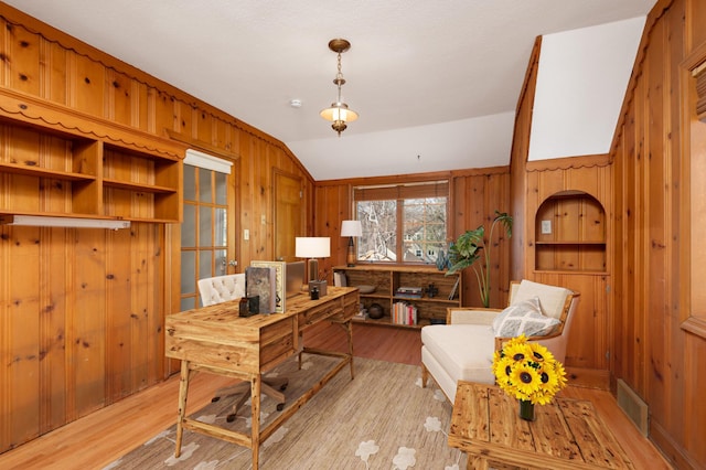 home office with light wood finished floors, visible vents, wood walls, and vaulted ceiling