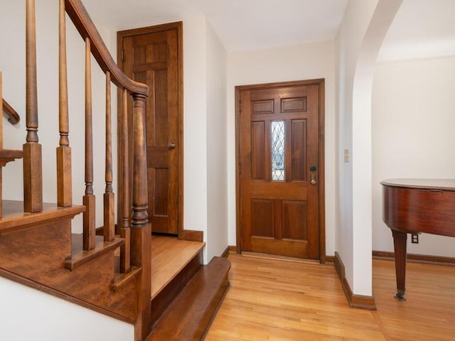 foyer entrance featuring stairs, light wood-style floors, arched walkways, and baseboards