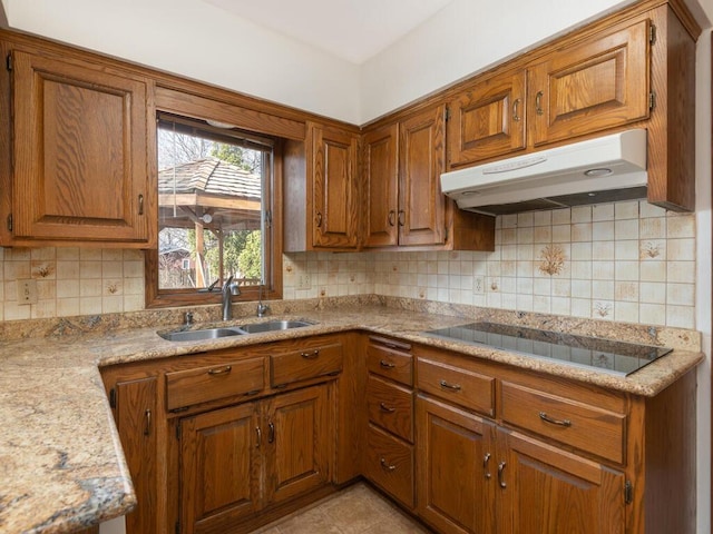 kitchen featuring black electric stovetop, brown cabinets, under cabinet range hood, and a sink