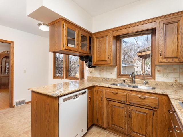 kitchen featuring light stone countertops, visible vents, white dishwasher, a sink, and brown cabinets