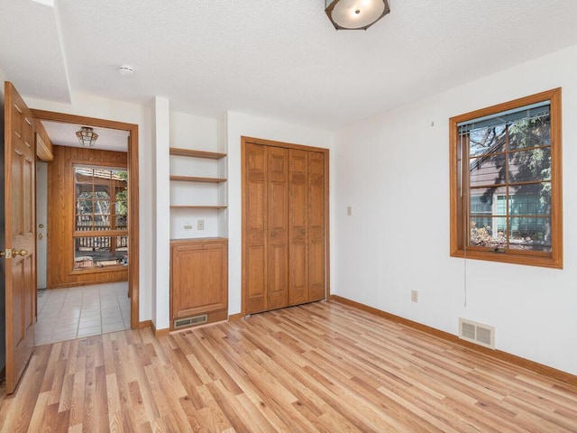 unfurnished bedroom with a closet, visible vents, a textured ceiling, and light wood-style floors