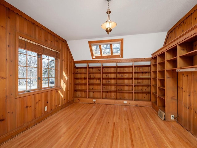 spare room featuring a healthy amount of sunlight, wood walls, a skylight, and light wood-style floors