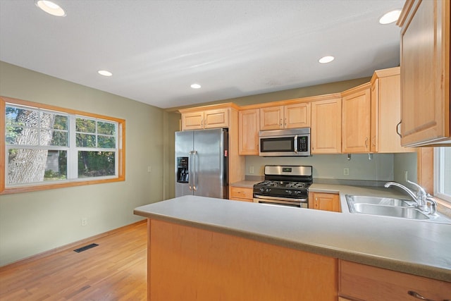 kitchen featuring light wood-type flooring, sink, kitchen peninsula, appliances with stainless steel finishes, and light brown cabinetry