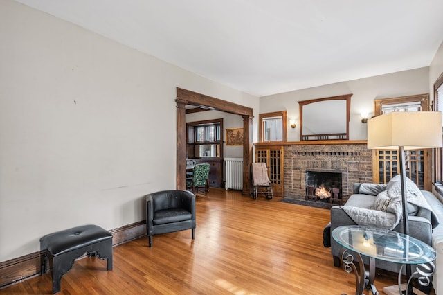 living room featuring ornate columns, radiator heating unit, wood-type flooring, and a brick fireplace