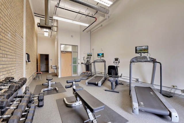 workout area featuring a towering ceiling and brick wall