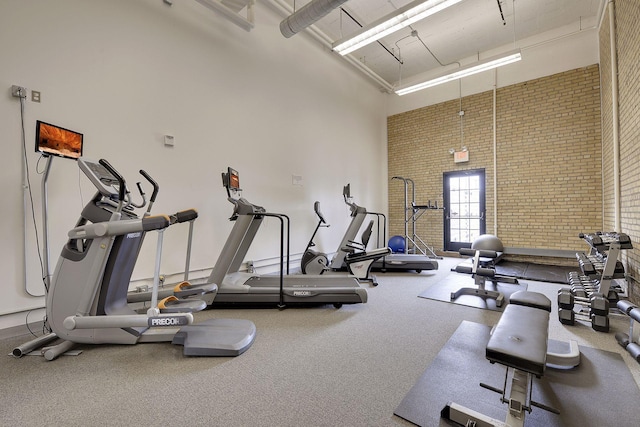 workout area featuring a towering ceiling and brick wall