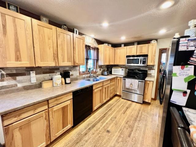 kitchen with light brown cabinetry, sink, light hardwood / wood-style floors, stainless steel appliances, and decorative backsplash