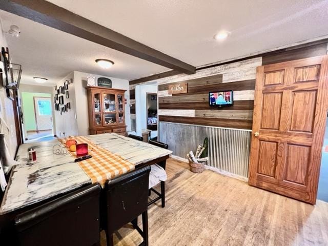 kitchen featuring beamed ceiling, wooden walls, and light hardwood / wood-style flooring