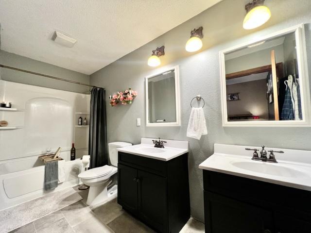 full bathroom with shower / bath combo, toilet, tile patterned flooring, vanity, and a textured ceiling