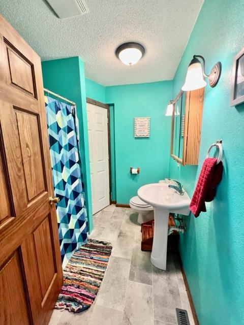 bathroom with a textured ceiling, toilet, and walk in shower