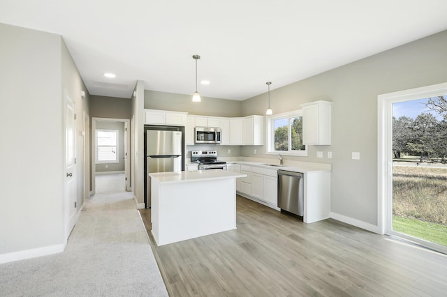 kitchen featuring stainless steel appliances, sink, pendant lighting, white cabinetry, and light hardwood / wood-style flooring