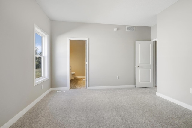 unfurnished bedroom featuring light carpet and connected bathroom