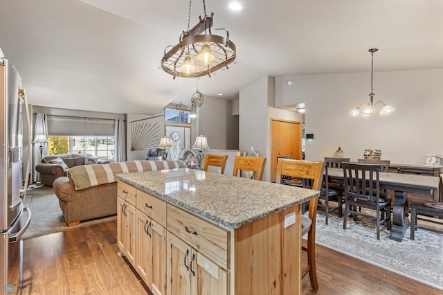 kitchen featuring lofted ceiling, a kitchen island, dark wood-type flooring, light stone counters, and stainless steel refrigerator