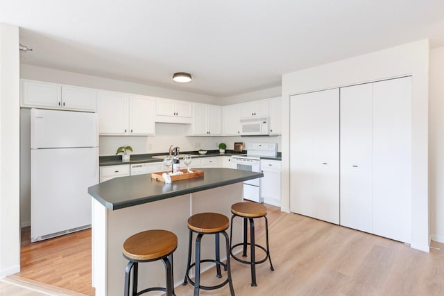 kitchen with white appliances, white cabinetry, light wood-type flooring, and a kitchen bar