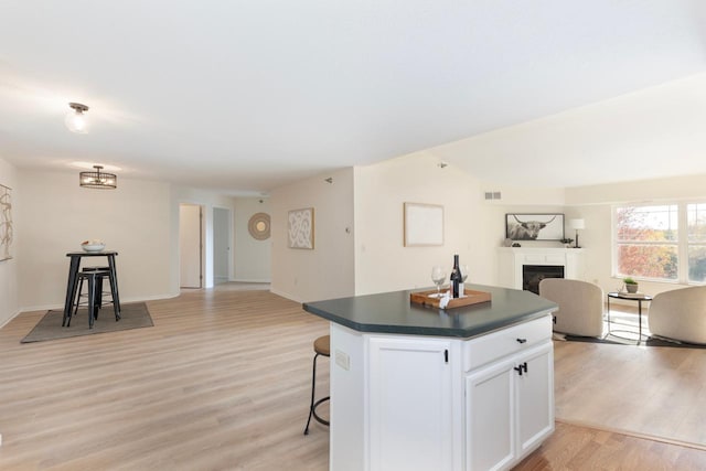 kitchen featuring white cabinets, a kitchen island, a kitchen bar, vaulted ceiling, and light wood-type flooring