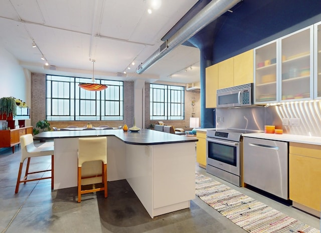 kitchen with hanging light fixtures, stainless steel appliances, concrete flooring, a kitchen bar, and a kitchen island