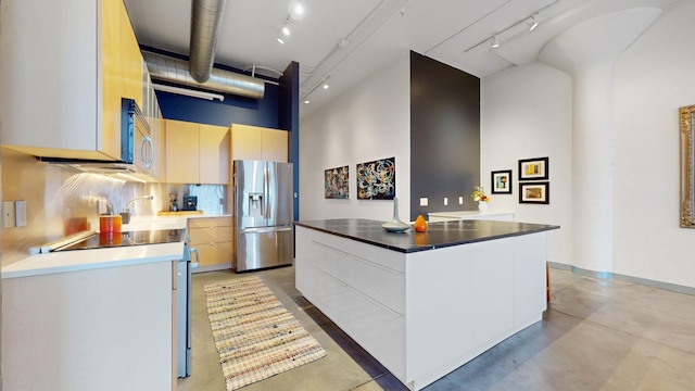 kitchen featuring a towering ceiling, tasteful backsplash, range, stainless steel fridge with ice dispenser, and a center island