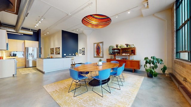 dining space featuring a towering ceiling, finished concrete floors, visible vents, and track lighting