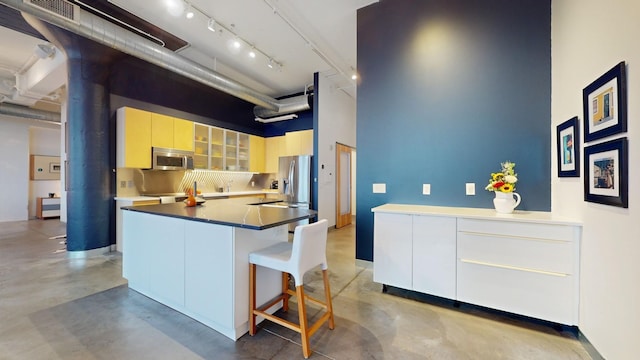 kitchen featuring stainless steel appliances, backsplash, finished concrete floors, modern cabinets, and a kitchen bar