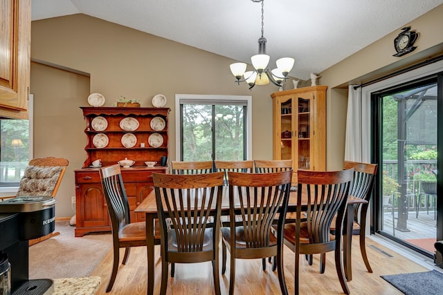 dining room with light wood-type flooring, lofted ceiling, a wealth of natural light, and a notable chandelier