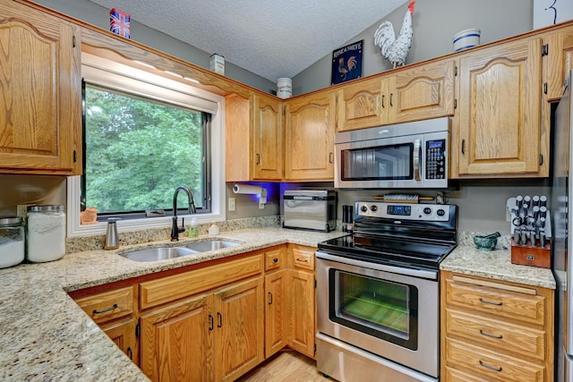 kitchen with sink, vaulted ceiling, a textured ceiling, appliances with stainless steel finishes, and light stone counters