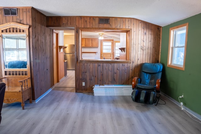 living area featuring a textured ceiling, wood walls, light hardwood / wood-style floors, and plenty of natural light