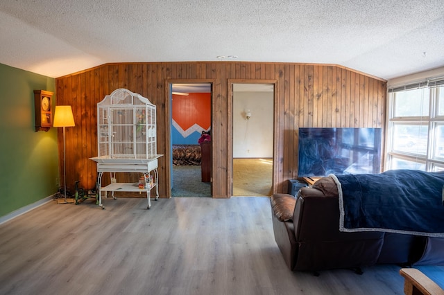 living room with wood-type flooring, wooden walls, lofted ceiling, and a textured ceiling