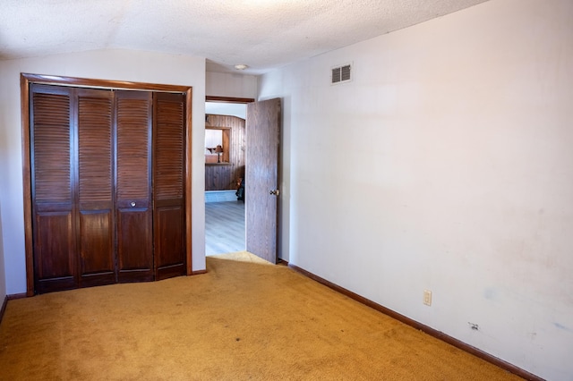 unfurnished bedroom with lofted ceiling, a closet, carpet flooring, and a textured ceiling