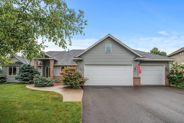 view of front of property with aphalt driveway, an attached garage, brick siding, a front lawn, and roof with shingles