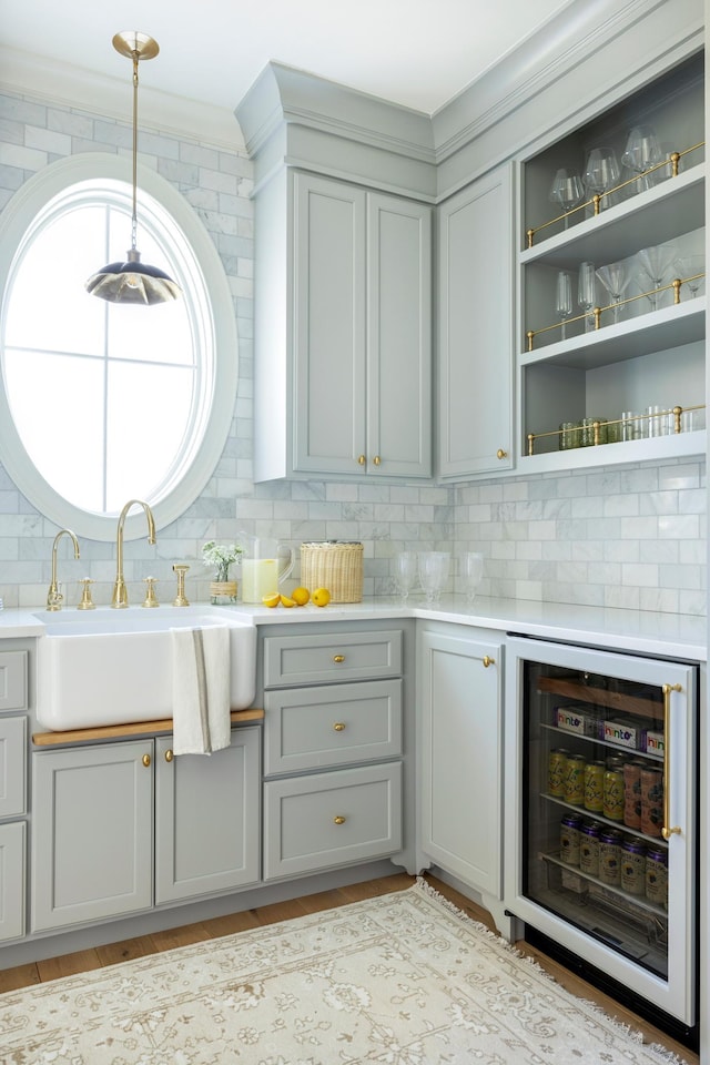 interior space with hanging light fixtures, gray cabinets, sink, and wine cooler