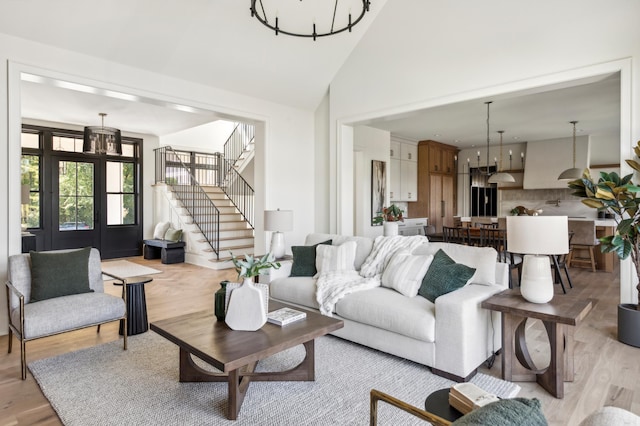 living room with high vaulted ceiling, a chandelier, and light wood-type flooring