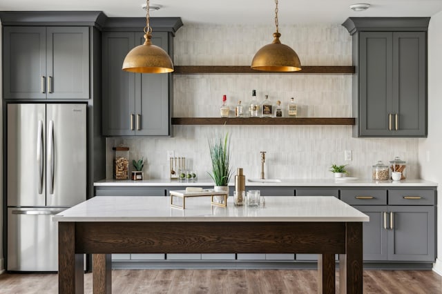 kitchen with pendant lighting, stainless steel refrigerator, gray cabinetry, and wood-type flooring