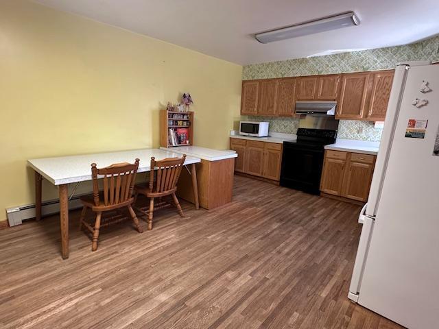kitchen featuring light countertops, white appliances, under cabinet range hood, brown cabinetry, and wood finished floors