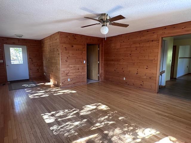 unfurnished living room featuring hardwood / wood-style floors, wooden walls, a ceiling fan, and a textured ceiling