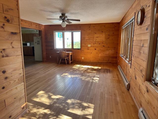 spare room featuring ceiling fan, wood-type flooring, baseboard heating, wood walls, and a baseboard heating unit