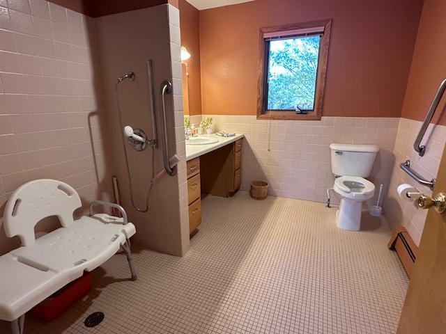bathroom featuring vanity, tile patterned floors, toilet, a wainscoted wall, and tile walls