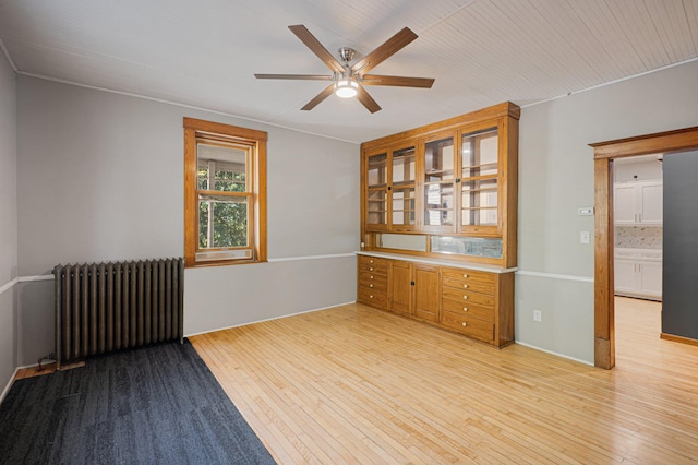 empty room with ceiling fan, light wood-type flooring, and radiator