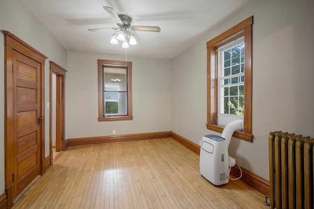 empty room featuring light wood-type flooring, ceiling fan, and radiator heating unit