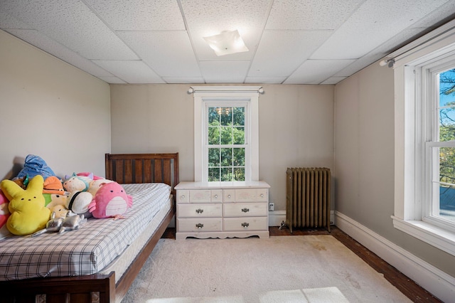 bedroom with a paneled ceiling, radiator heating unit, and hardwood / wood-style flooring