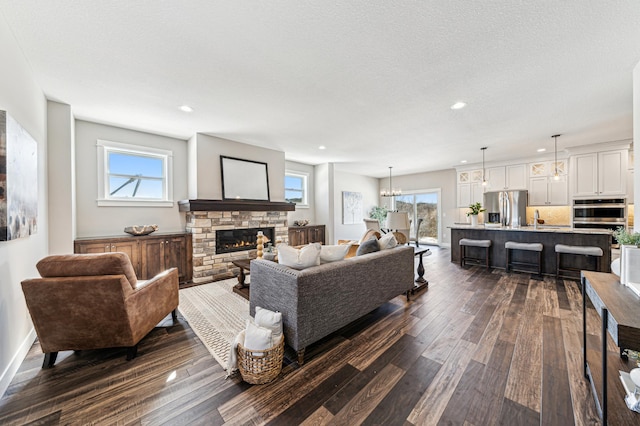 living room with recessed lighting, a textured ceiling, dark wood-style flooring, and a stone fireplace