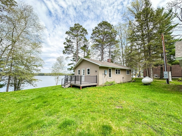 rear view of property featuring a lawn and a deck with water view