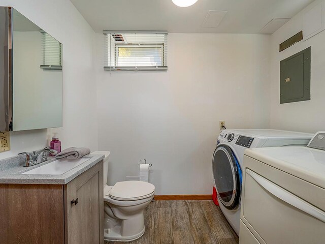 laundry area with washing machine and dryer, electric panel, sink, and wood-type flooring