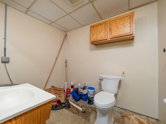 bathroom with concrete floors, a drop ceiling, vanity, and toilet